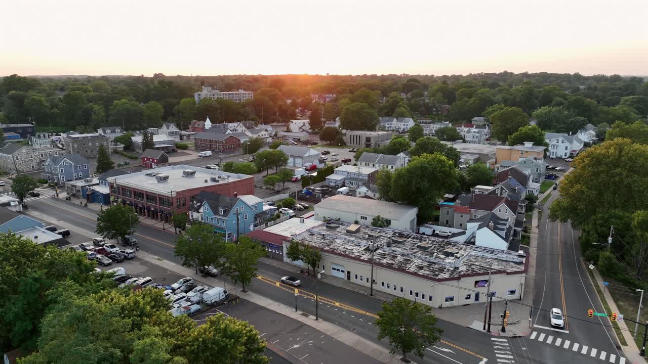 Peaceful sunrise of small American town. Main Street with cars along shops and stores in historic city of Trenton, New Jersey. Green trees and housing area in background. Aerial rising wide shot