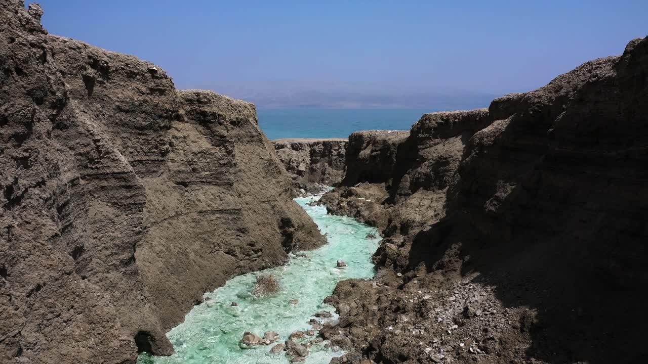 Dead Sea Hot Springs dramatic aerial fly in through desert canyon landscape over fast running crystal clear warm waters on a sunny day