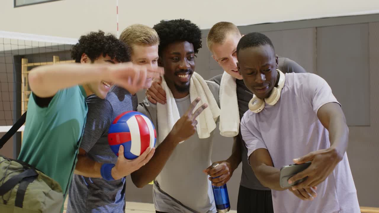 Vielfältiges männliches Volleyballteam trifft sich nach dem Training im Fitnessstudio, einer zeigt sein Telefon, macht ein Selfie und jubelt