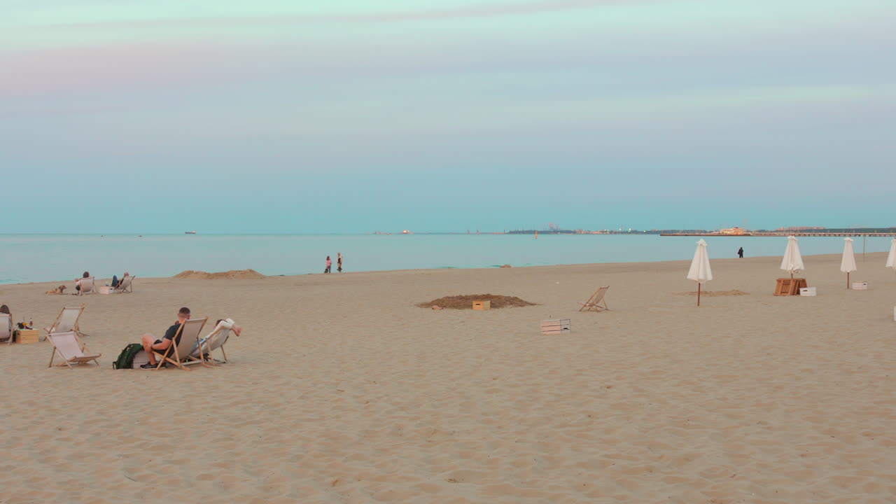 People relaxing on Sopot beach at dusk with pastel sky and calm waters in the background