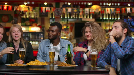 una alegre compañía de 7 amigos se comunican en un bar bebiendo cerveza y riendo contando historias.