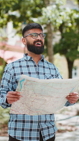 Indian-man-tourist-exploring-city-street-sightseeing-holding-paper-map-check-direction-searching-way