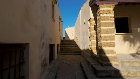 a narrow alleyway in cádiz with traditional stone stairs leading up between old buildings, cast in the golden light of the sun