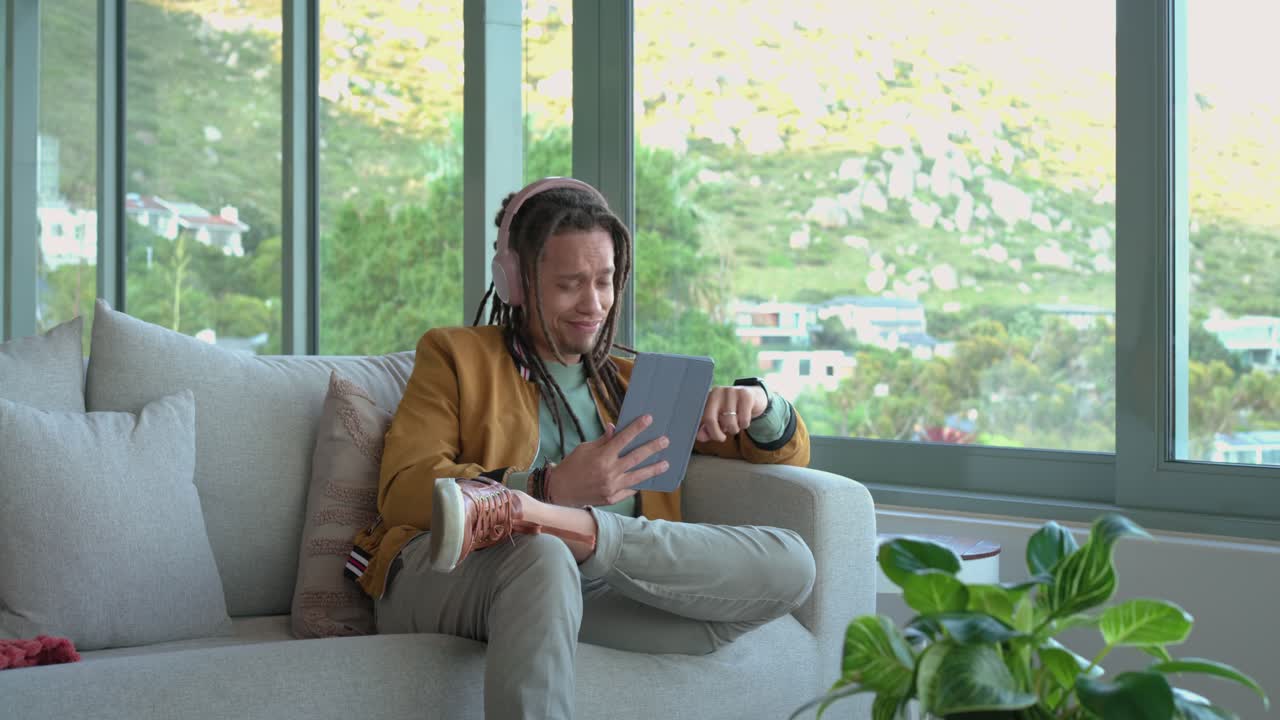 Mid adult man rubbing temple then grabbing tablet and scrolling to relieve confusion on sofa