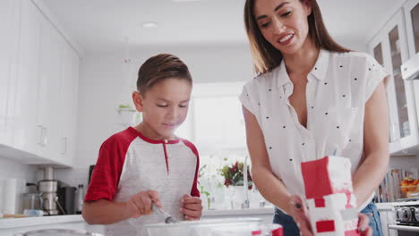 pre-adolescente niño hispano y su madre haciendo mezcla de pasteles en la cocina añadiendo harina, de cerca, ángulo bajo