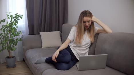 Blonde-Frau-Entspannt-Sich-Auf-Der-Couch,-Während-Sie-Zu-Hause-Mit-Dem-Laptop-Videoanrufe-Tätigt