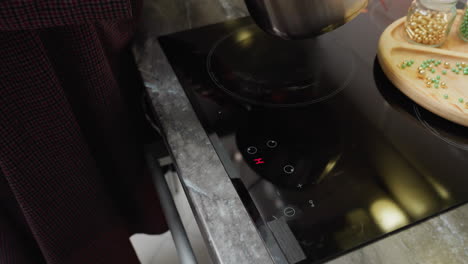vista parcial de una persona apagando la estufa eléctrica mientras otra persona levanta la olla con líquido verde, moviendo en la estufa de inducción, cocina moderna con utensilios de cocina y cocción en acción