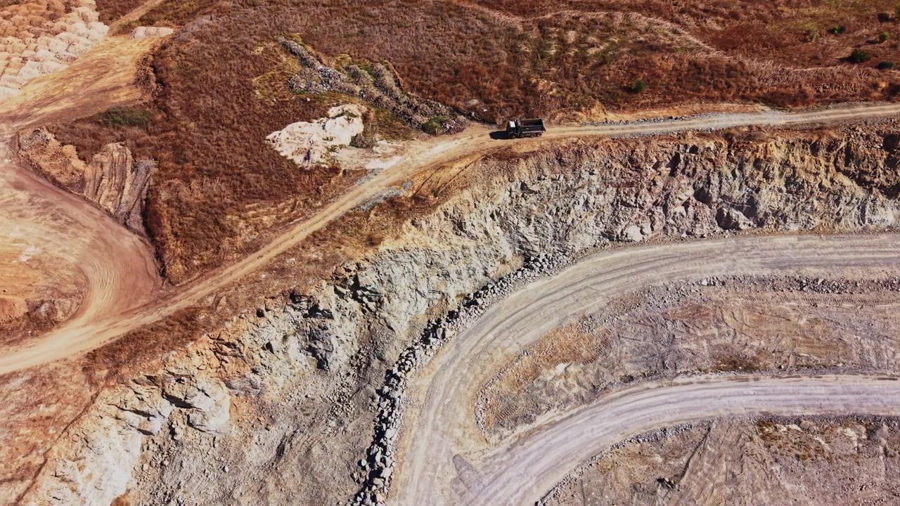 Large excavation site with a truck on a dirt road in a dry landscape