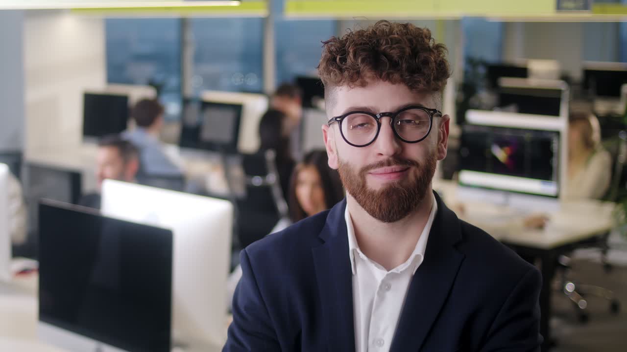Retrato de un jefe alegre con chaqueta y gafas, mirando a la cámara y sonriendo. Atractivo hombre caucásico, líder de equipo en una oficina moderna de empresa.
