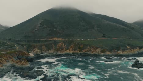 Car-road-at-the-side-of-a-mountain-next-to-the-coast,-majestic-areal-view