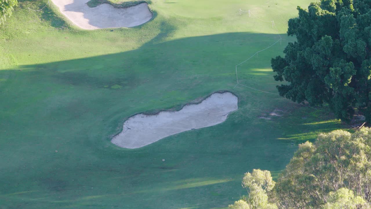Drone captures sweeping views of a lush golf course with sand bunkers and trees during golden sunset hour