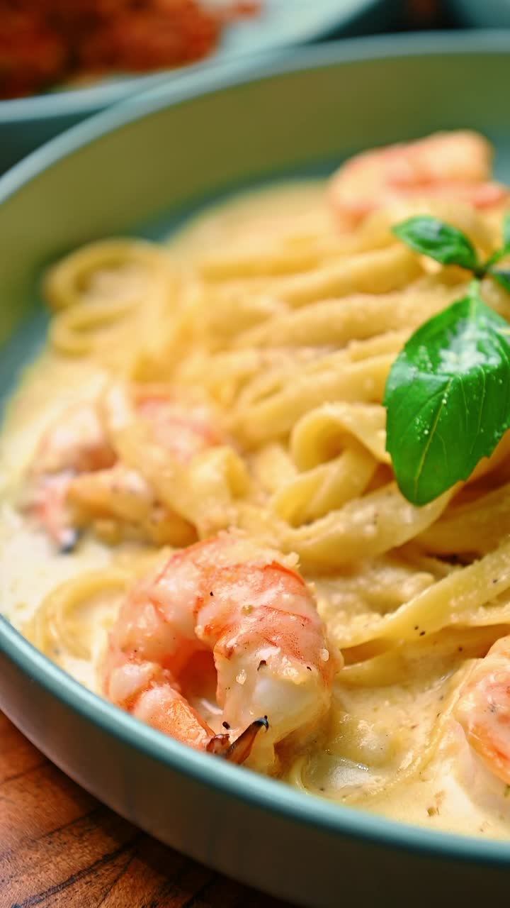 Primo piano di una forchetta che raccoglie gamberi da pasta cremosa. Persona che usa una forchetta d'argento per sollevare gamberi cotti da fettuccine in salsa bianca con una foglia di basilico.