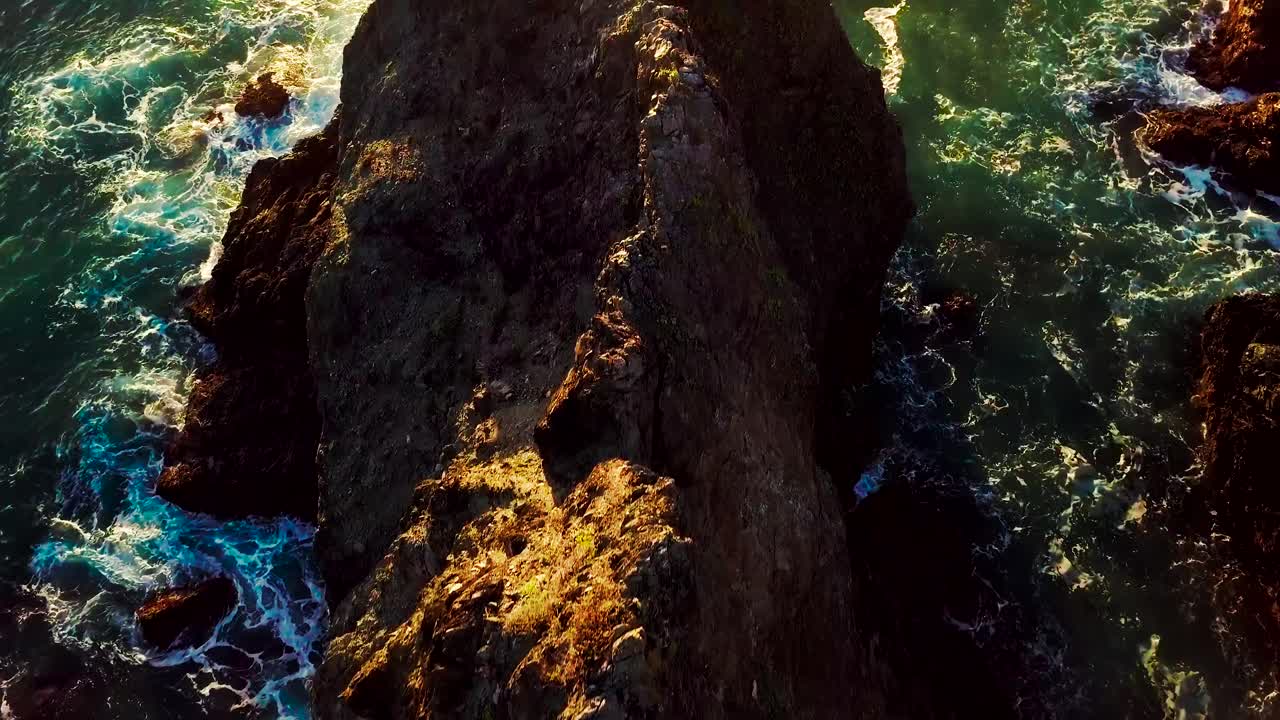 O sol poente ilumina ondas verdes do oceano quebrando em penhascos rochosos em Big Sur, Califórnia