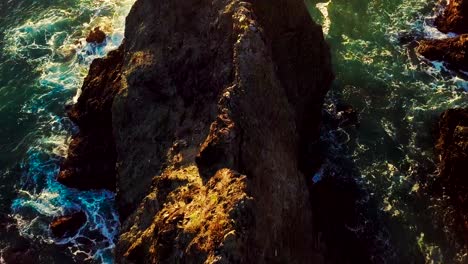 Setting-sun-lights-up-green-ocean-waves-crashing-into-rocky-cliffs-in-Big-Sur-California