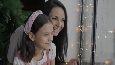 mother and daughter looking out a window at christmas