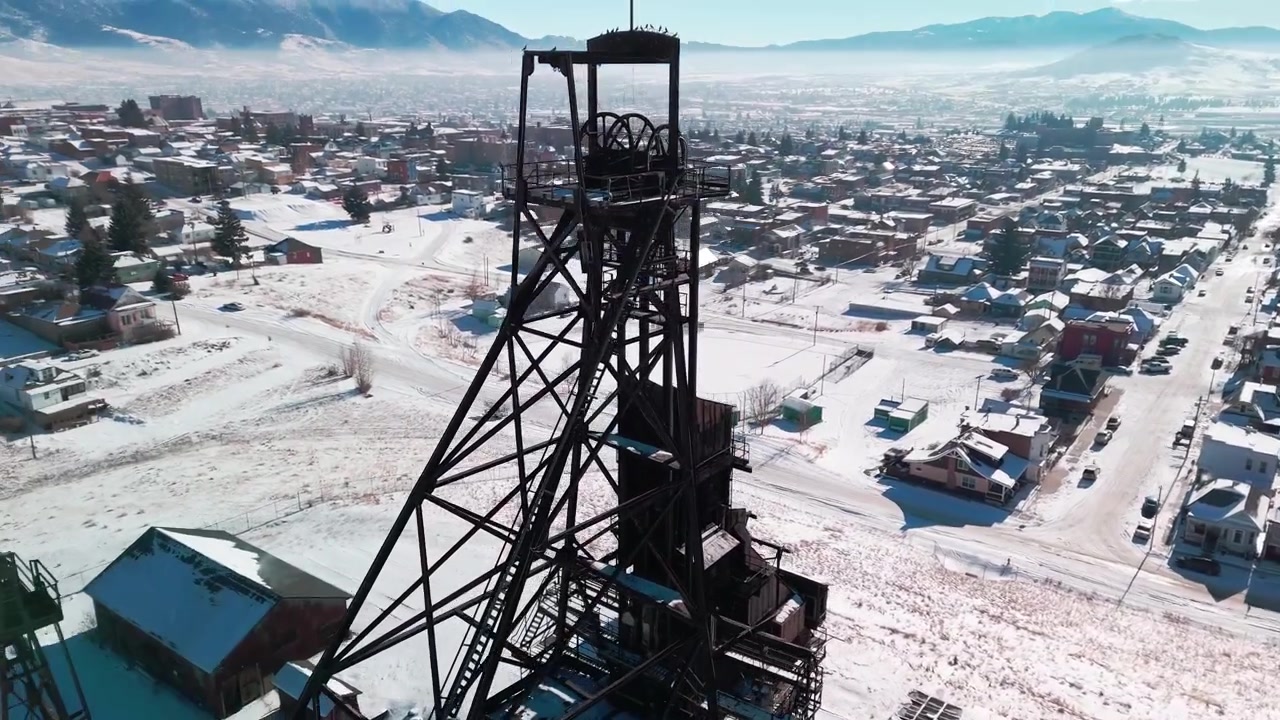 aerial drone perspective showcasing the industrial legacy of Butte, Montana, focusing on preserved mining equipment, rusted steel structures, and the raw landscape of the region snow covered in winter