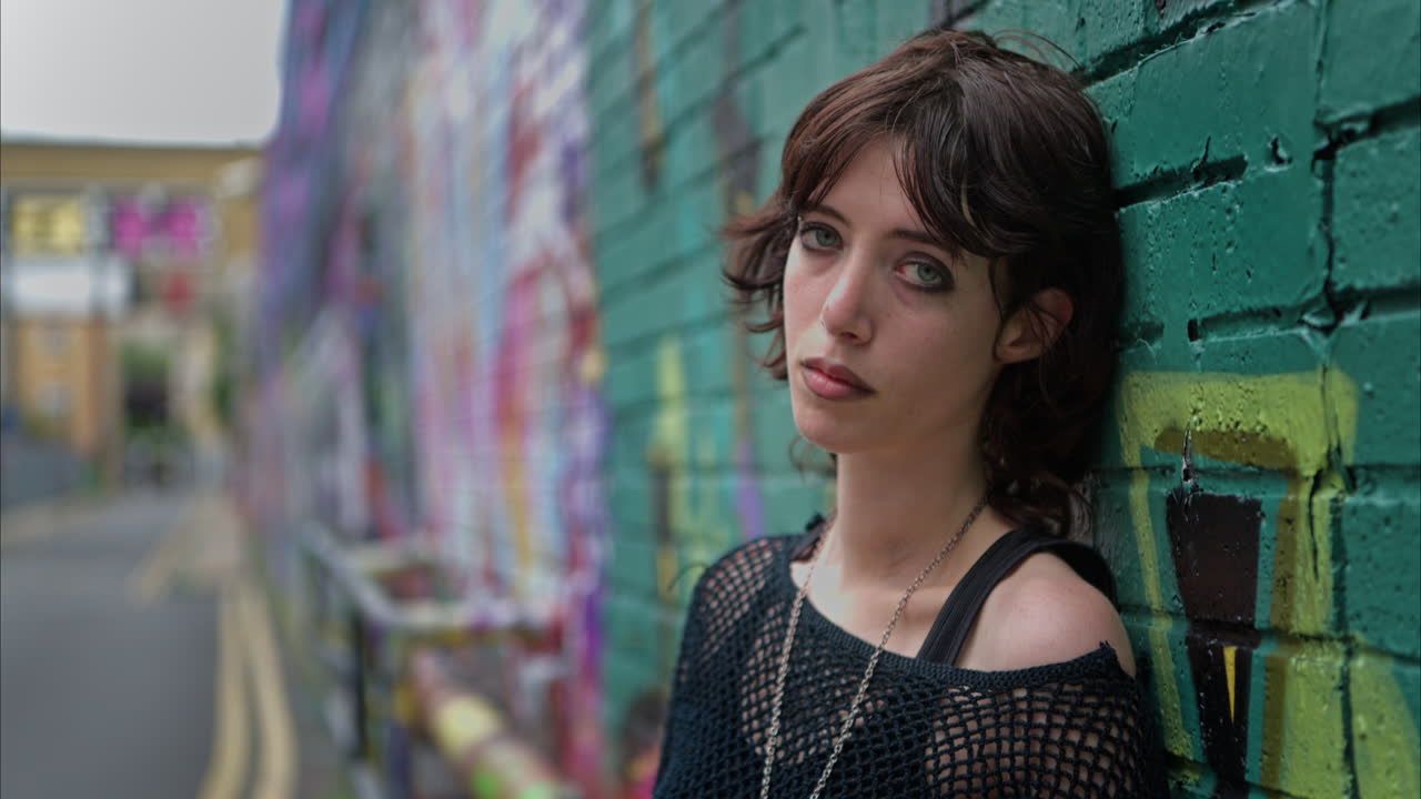 Close Up Outdoor Fashion Portrait Of Young Alternative Style Woman Leaning Against Graffiti Covered Wall In London City Street UK In Real Time