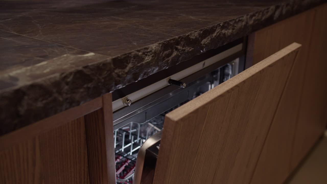 disparo de seguimiento de la mano abriendo un lavaplatos oculto en una cocina moderna con encimeras de mármol y gabinetes de madera
