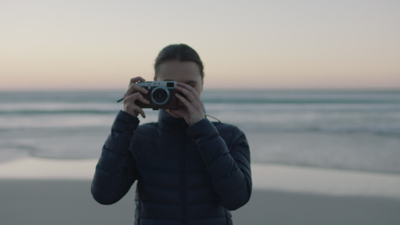 ritratto di una giovane donna sicura di sé che scatta una foto usando una fotocamera retro godendosi la tranquilla spiaggia al tramonto