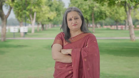 Confident-Indian-old-woman-standing-crossed-hands-in-park