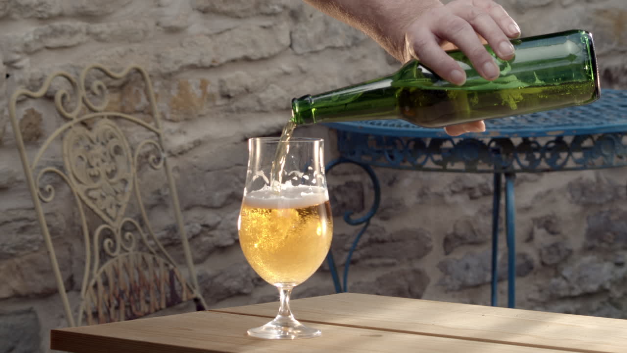 brazo masculino descuidadamente vierte y derrama cerveza de botella a vaso