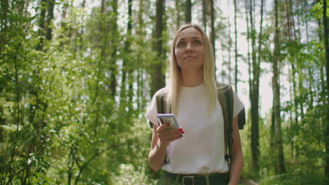 attractive woman relax in forest and using smartphone outdoors. woman hiking in the forest and typing message on smartphone. solo female hiker using smart phone.