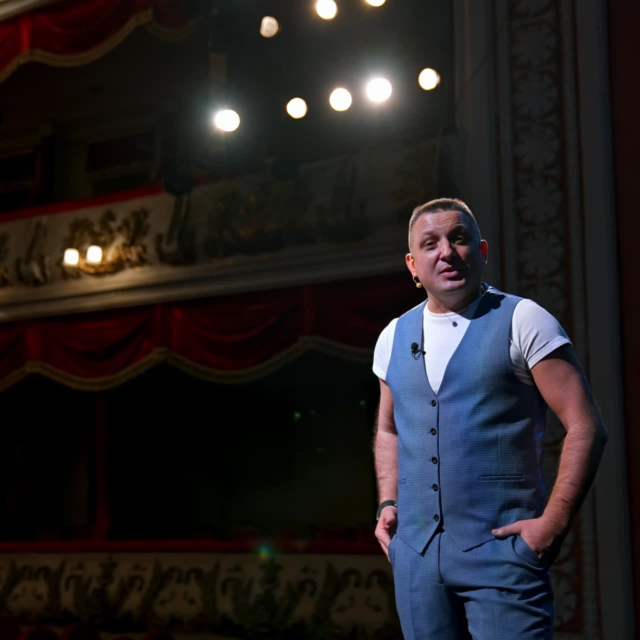 Showman entertains the audience under the light, front view. Big stage. Serious performer speaks from the stage. Hands in pockets