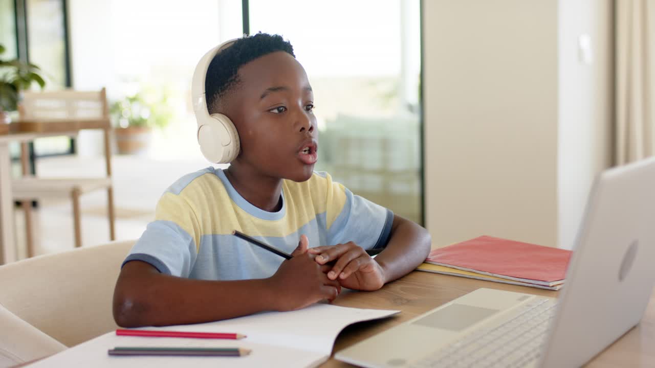 African American boy raising hand listening and speaking to laptop in online lesson at study table