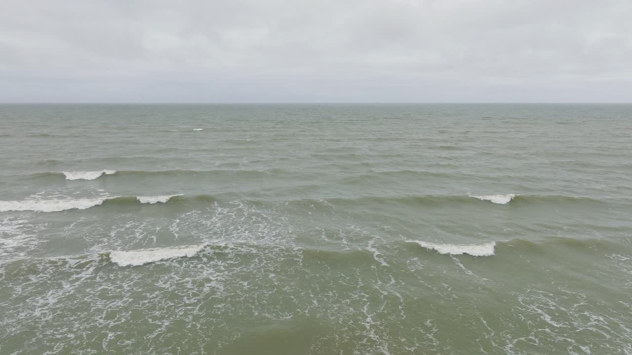 흐린 날 발트해 연안의 공중 전망, 오래된 목조 부두, 하얀 모래 해변, 해안에 부딪히는 큰 폭풍우, 기후 변화, 넓은 드론 샷이 뒤로 낮게 움직입니다.