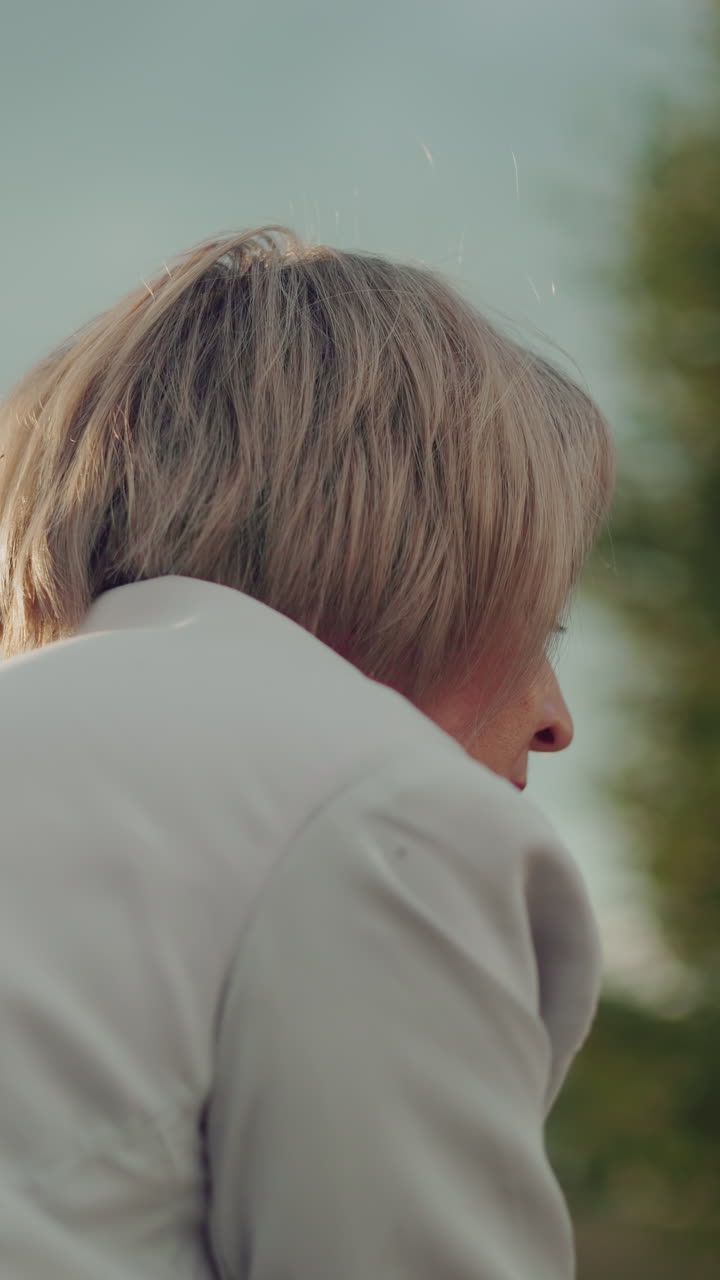 mujer de mediana edad acostada con una expresión enfocada, mirando hacia adelante, la luz natural suave destaca su cara contra un cielo nublado, con árboles en el fondo