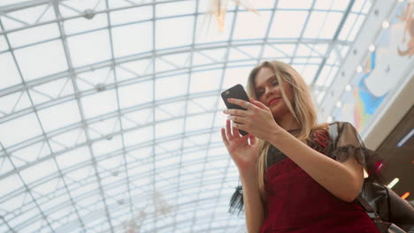 una hermosa chica baja por la escalera mecánica y habla por teléfono en el centro comercial.