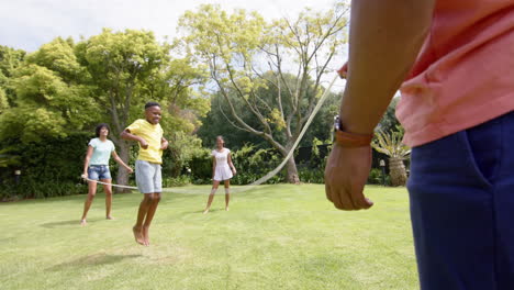 Felices-Padres-Afroamericanos,-Hijo-E-Hija-Saltando-En-Un-Jardín-Soleado,-Cámara-Lenta