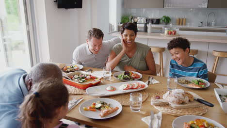 Familia-De-Raza-Mixta-Multigeneracional-Comiendo-Comida-Alrededor-De-La-Mesa-En-Casa-Juntos