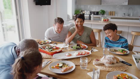 familia de raza mixta de varias generaciones comiendo alrededor de la mesa en casa juntos