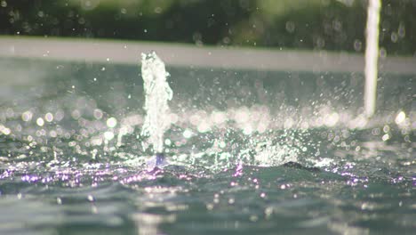 closeup of water drops splashing from fountain inside liquid surface reflecting colorful light