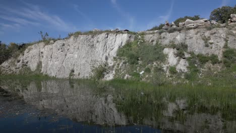 flight-in-reverse-with-a-drone-visualizing-a-wall-of-white-earth-and-on-the-ground-there-is-water-dammed-with-aquatic-plants-we-see-a-blue-sky-with-light-clouds-on-a-spring-afternoon-Avila-Spain