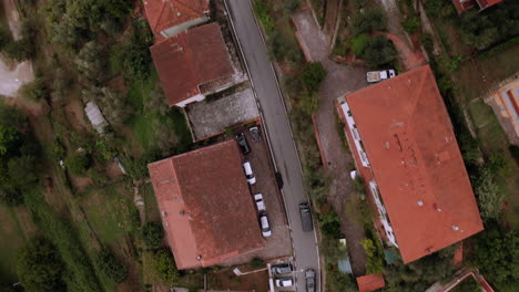 Drone-following-a-black-car-at-birds-eye-view,-driving-through-a-city-with-orange-roofs-surrounded-by-nature,-Florence,-Italy