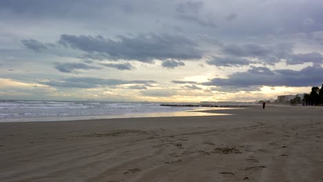 hombre en la distancia camina sobre la arena de la playa disfrutando del hermoso paisaje durante la puesta de sol
