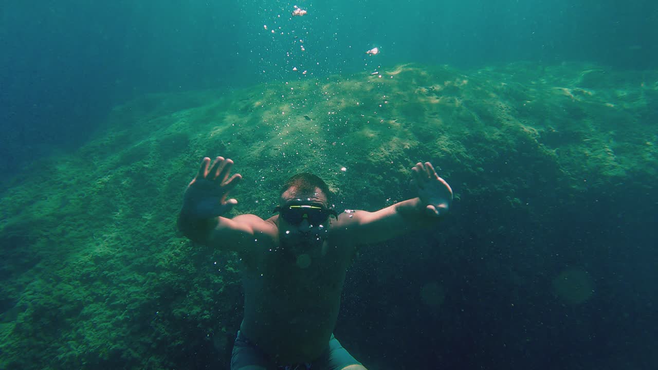 hombre con los brazos abiertos buceando y nadando bajo el agua en apnea con máscara de buceo en agua de mar cristalina color turquesa
