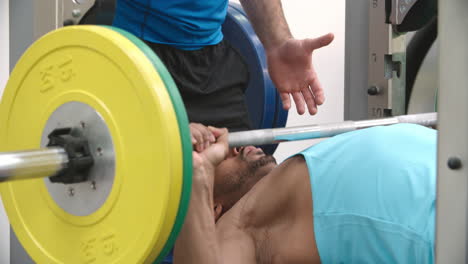 entrenador ayudando a un hombre presionando barras en un gimnasio