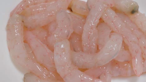 rotating raw pink shrimp on white background, closeup from above