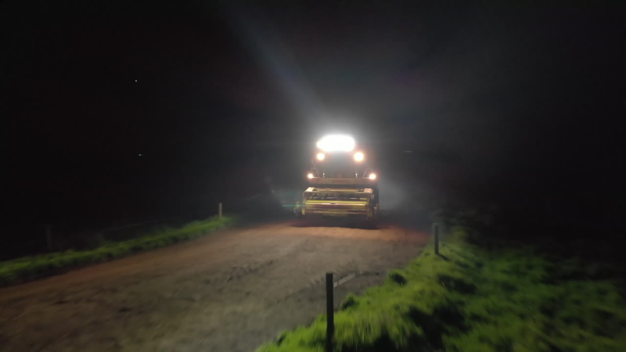 Aerial pullback shot of farming vehicle driving towards camera then reveal more vehicles behind