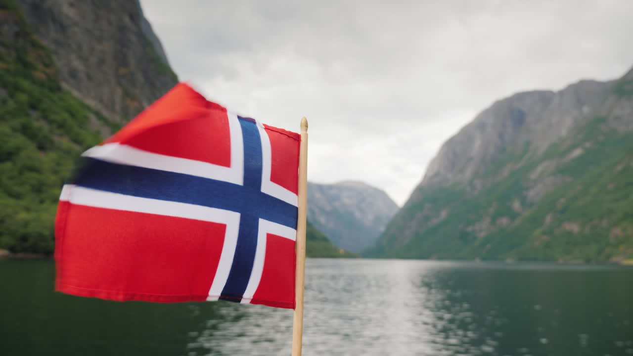 la bandera noruega ondea en el viento contra el telón de fondo de un majestuoso crucero por los fiordos o