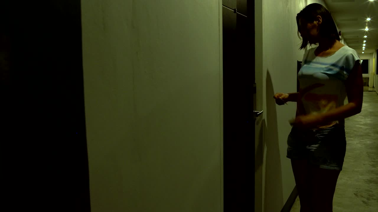 한 여성이 호텔의 복도를 따라 걸어가서 키카드를 적용하고 방에 들어갑니다.