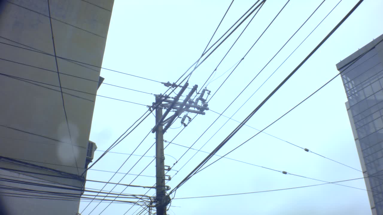 look up slight movement view of an old vintage simple electricity pole with complicated cable lines across hanging in the sky horizontal and vertical onto the apartment building in cloudy gloomy day