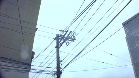 look up slight movement view of an old vintage simple electricity pole with complicated cable lines across hanging in the sky horizontal and vertical onto the apartment building in cloudy gloomy day