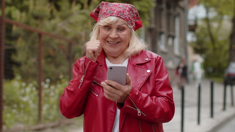 feliz ganadora excitada mujer mayor usa teléfono inteligente celebrando ganar buenas noticias de mensaje en la calle de la ciudad