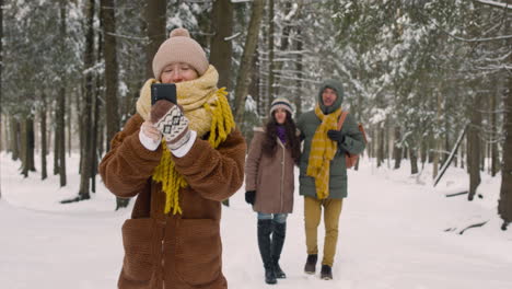 Front-View-Of-A-Girl-Taking-Photos-With-Smartphone-In-Winter-Clothes-In-Snowy-Forest