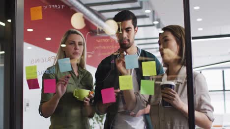 diversos colegas de oficina escribiendo en tablero de vidrio y discutiendo juntos en una oficina moderna