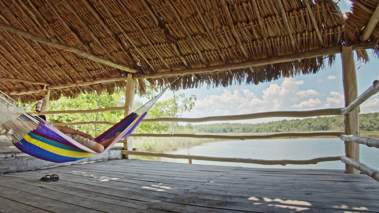 Slow motion of man having a nap on hammock inside a hut in Chunyaxche, Quintana Roo, Mexico. Wide panning shot.